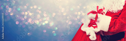 Santa holding a present box from a red sack on a shiny light background
