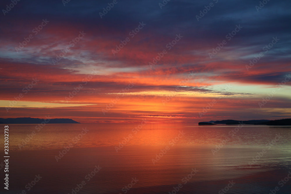 Bay at sunset. Bright sunrise landscape in sea. Flaming colors of early morning. Dawn silence on lake.