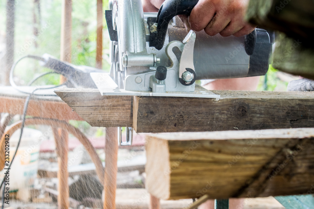 A man works with his hands and a construction tool. Electric saw. Work on wooden boards. To cut the materials. Fine shavings flying in all directions.