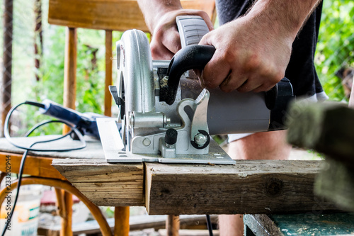 A man works with his hands and a construction tool. Electric saw. Work on wooden boards. To cut the materials. Fine shavings flying in all directions.