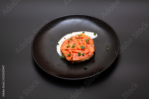 Black plate with smoked salmon on a potato pancake with sauce. Tasty snack