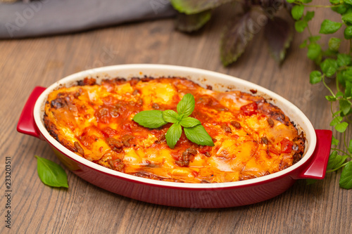 Italian food. Hot tasty freshly baked lasagna served with basil herb on wooden table.