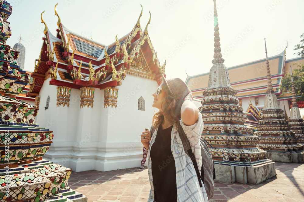 Fototapeta premium Young beautiful happy smiling european woman in a hat and glasses at a buddhist temple in Bangkok traveling to southeast Asia
