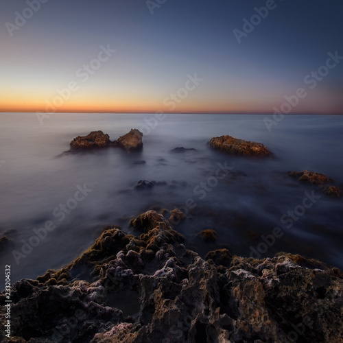 beautiful sunrise at sea shore and wet rocks in water. soft light, pink sky. Square landscape