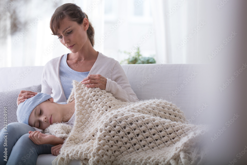 Caregiver supporting sleeping sick kid with cancer wearing headscarf in the hospice
