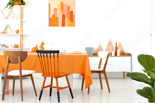 Fotografie Three different chairs placed by the long dining table with orange tablecloth an