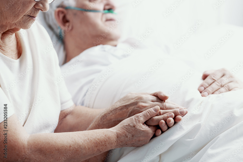 Senior man with lung cancer laying in hospice bed supporting by his elderly wife, photo with copy space
