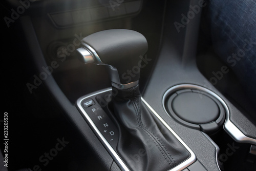 Car interior indoor. Black leather automatic gearbox with chrome button and sun rays, round ashtray  photo
