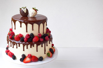 Two-tiered wedding cake in chocolate, with slices strawberries, raspberries, blackberry, decorated with figures of the bride and groom on a white background.