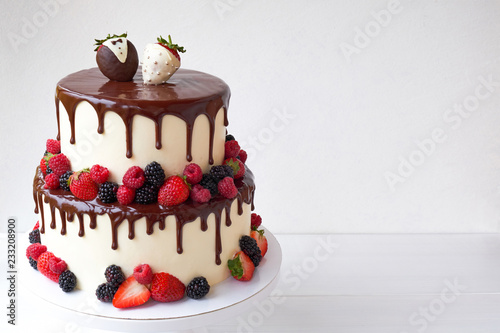 Two-tiered wedding cake in chocolate, with slices strawberries, raspberries, blackberry, decorated with figures of the bride and groom on a white background.