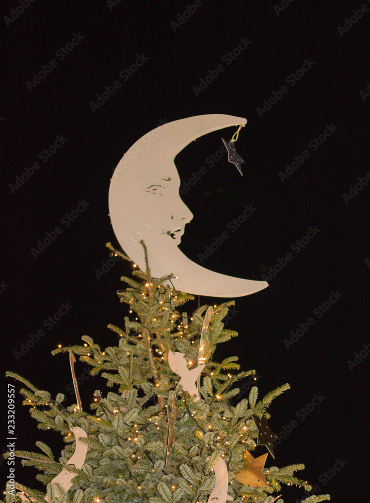 Vertical image: top of high Christmas tree is decorated with an image of beautiful half-moon and star on a background of night dark sky. Concept: Merry Christmas and Happy New Year holidays.
