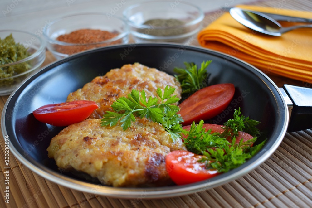 Delicious fried cutlets with tomatoes and herbs in a frying pan.