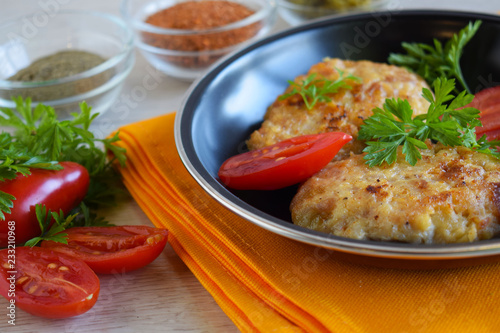 Delicious fried cutlets with tomatoes and herbs in a frying pan.