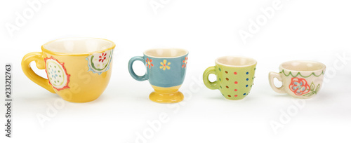 Four pretty ceramic teacups in a row on white background. Varying colours, patterns and sizes in descending order. Cheerful bright pastel colours. In a banner shape.