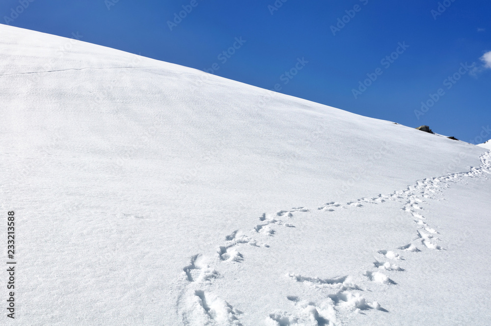footsprint on the hill covered with snow under blue sky footsprint on the hill covered with snow under blue sky