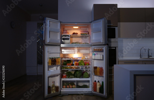 Open refrigerator filled with food in kitchen at night