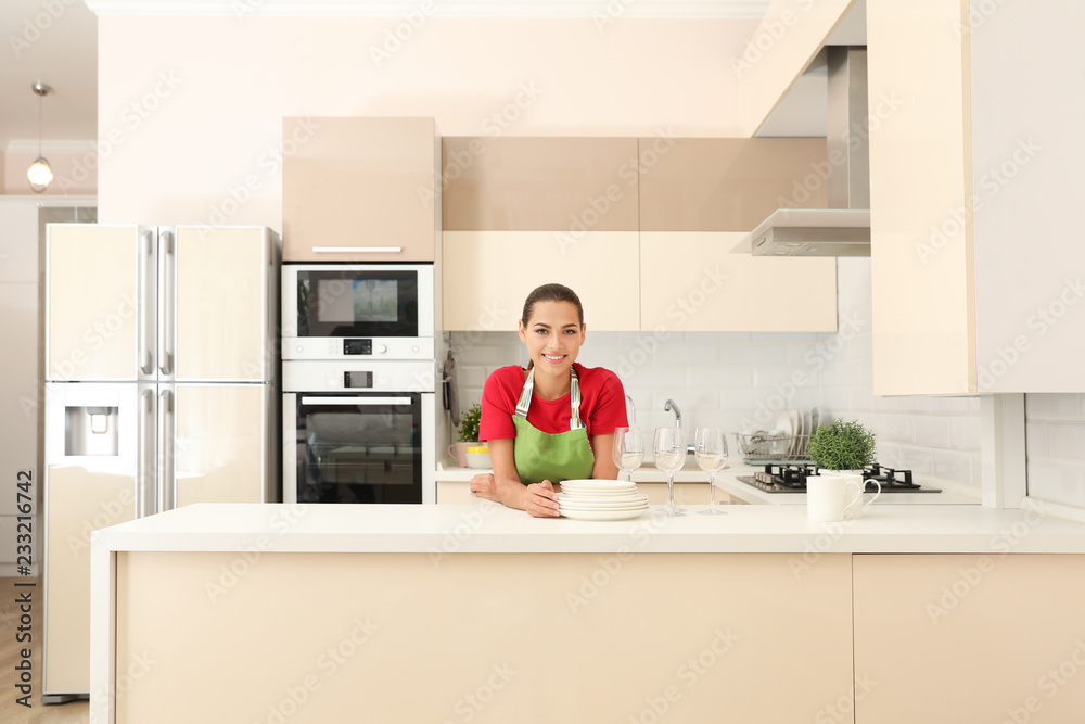 Beautiful young woman with clean dishes in kitchen