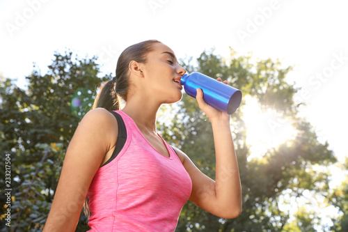 Young sporty woman drinking from water bottle in park on sunny day