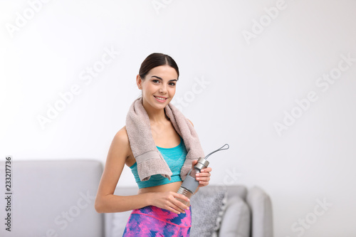 Beautiful young woman in sportswear with towel and bottle of water indoors