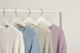 Collection of warm sweaters hanging on rack against white brick wall