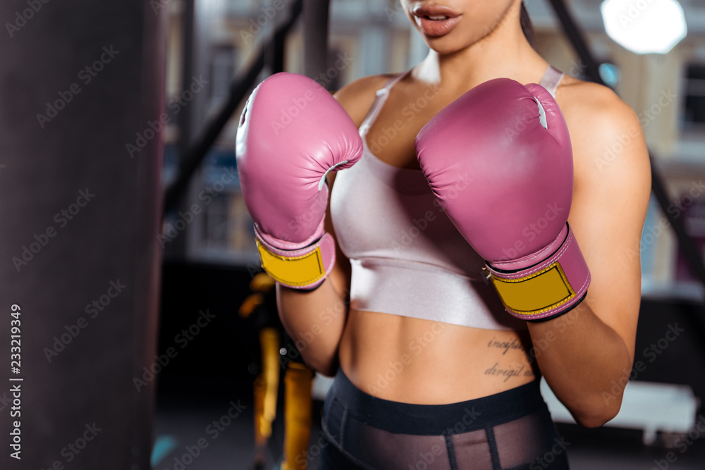 Partial view of strong girl in boxing gloves practicing boxing in gym