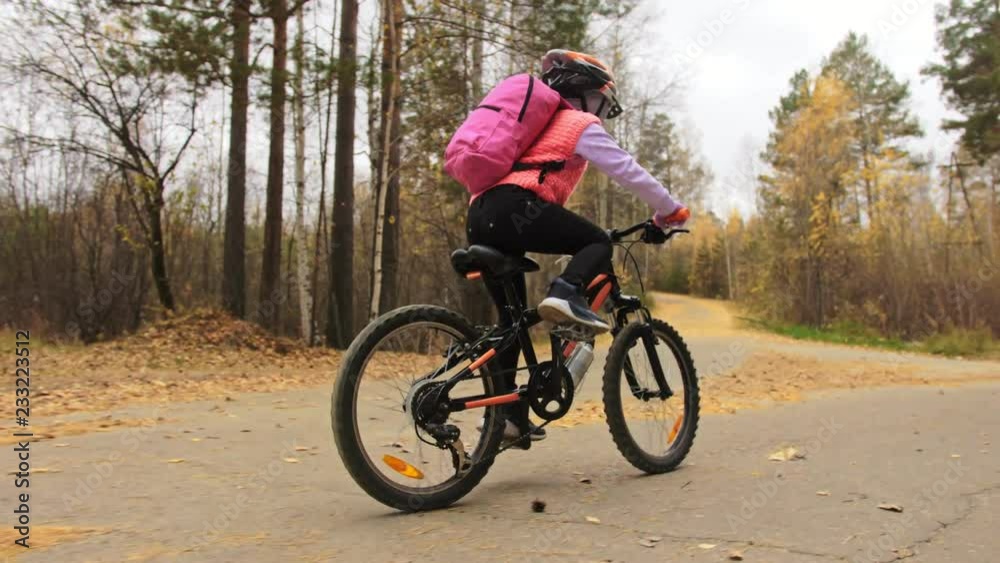 One caucasian children rides bike road in autumn park. Little girl riding black orange cycle in forest. Kid goes do bicycle sports. Biker motion ride with backpack and helmet. Mountain bike hardtail. One caucasian children rides bike road in autumn park. Little girl riding black orange cycle in forest. Kid goes do bicycle sports. Biker motion ride with backpack and helmet. Mountain bike hardtail.