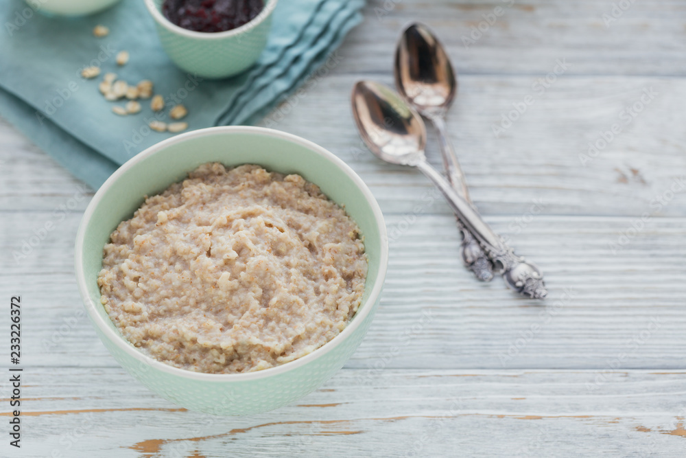 Oatmeal porridge bowl on the white wooden background.