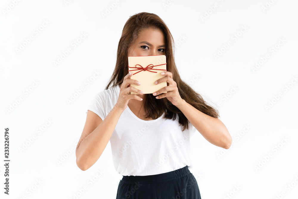 Cheerful girl covering face by gift. Young woman showing present box with copy space on top. Giving gifts season concept Cheerful girl covering face by gift. Young woman showing present box with copy space on top. Giving gifts season concept