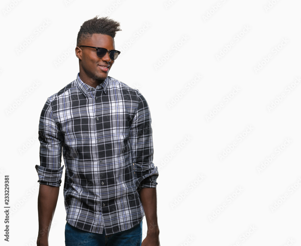 Young african american man wearing sunglasses over isolated background looking away to side with smile on face, natural expression. Laughing confident. Young african american man wearing sunglasses over isolated background looking away to side with smile on face, natural expression. Laughing confident.