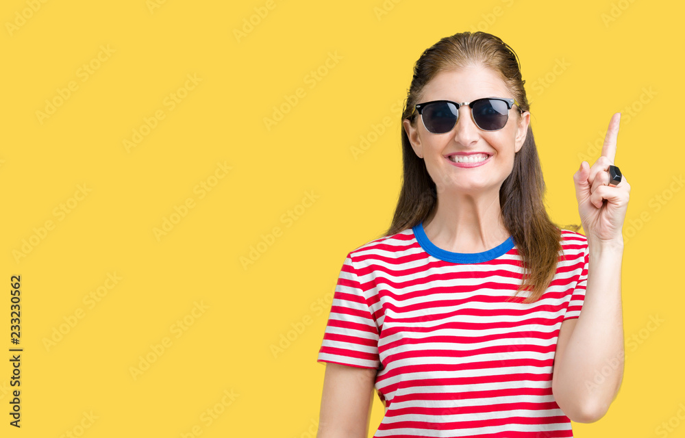 Fototapeta premium Middle age mature woman wearing sunglasses over isolated background pointing finger up with successful idea. Exited and happy. Number one.