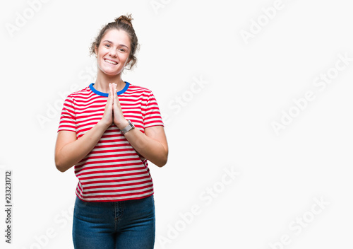 Beautiful brunette curly hair young girl wearing casual look over isolated background praying with hands together asking for forgiveness smiling confident. © Krakenimages.com