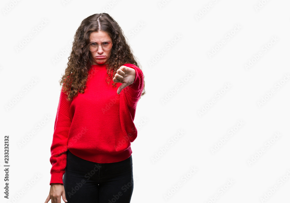 Beautiful brunette curly hair young girl wearing glasses and winter sweater over isolated background looking unhappy and angry showing rejection and negative with thumbs down gesture. Bad expression.