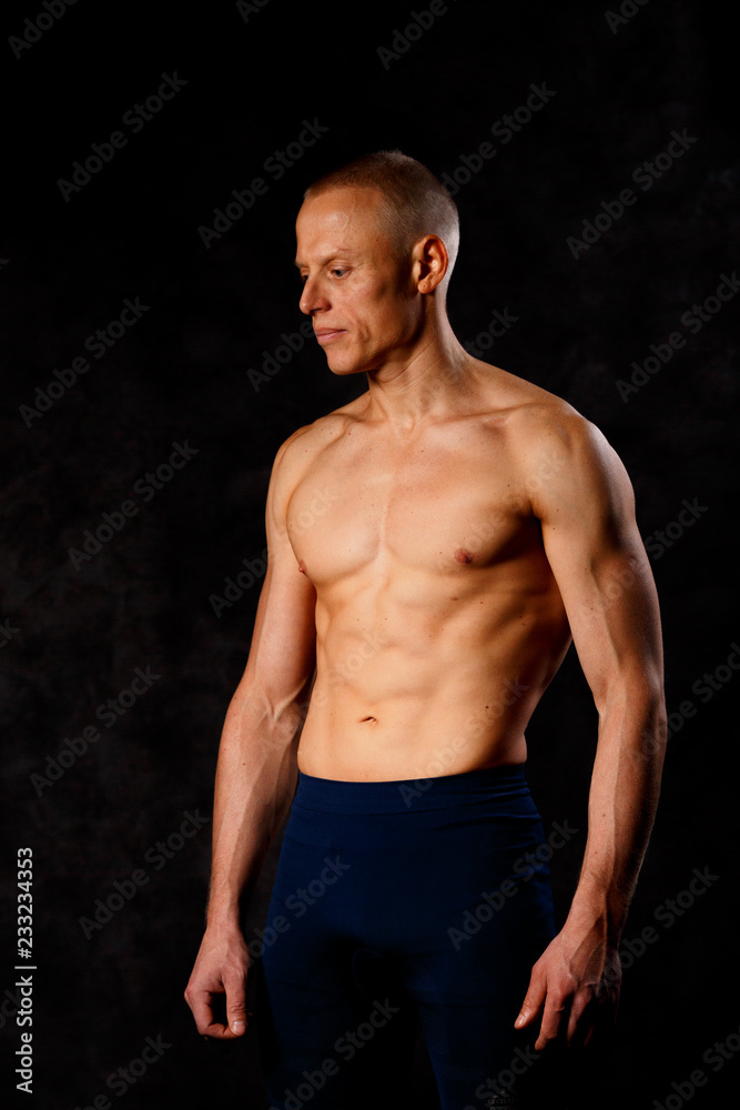 Handsome muscular man posing on dark background.
