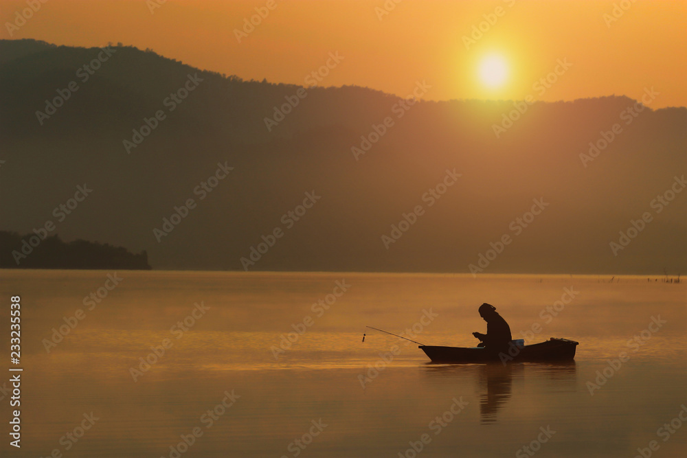 Silhouette lonely fishing man sitting in his boat and look smart phone with sunset sky and selective focus, Background for weekend travel or recreation or relax activity after working hard, Thailand.