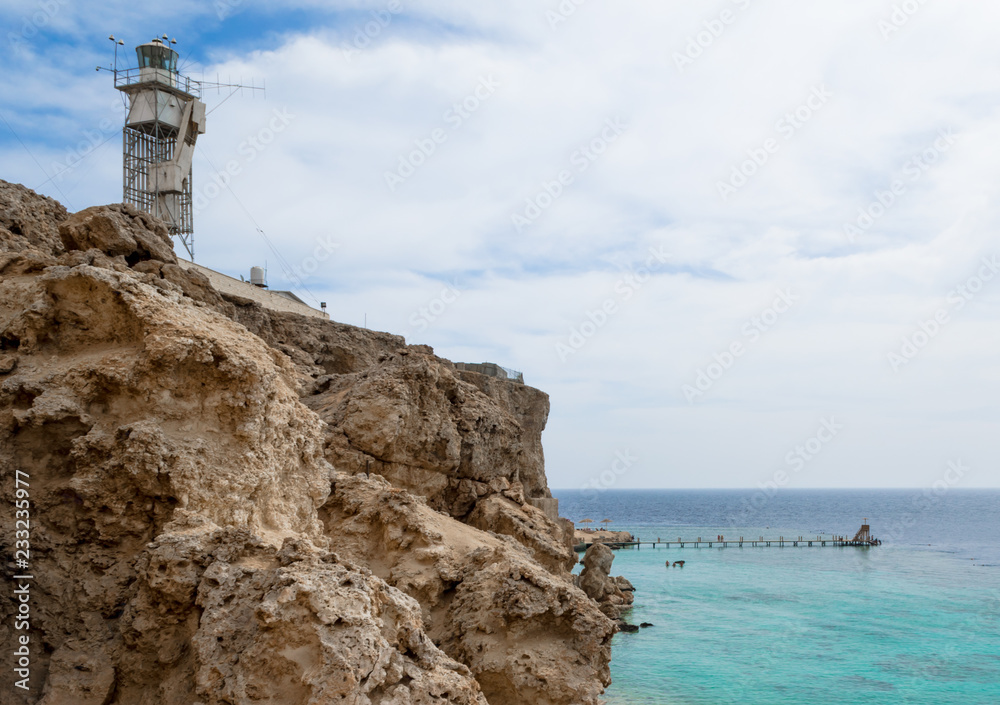 lighthouse on a stone rock on the shore of the Red Sea. Egypt on a background of blue sky and clouds