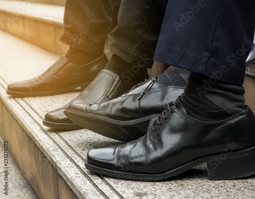 Leather shoes of two business people sit on the stairs.