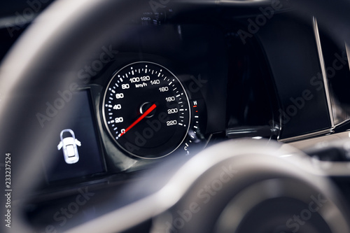 Close-up of the speedometer on the dashboard of a modern expensive car. The dashboard illumination is reflected. Front background is blurred