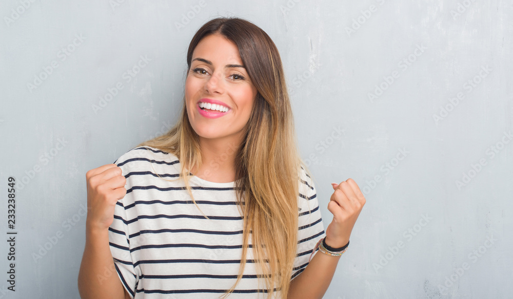 Young adult woman over grunge grey wall wearing navy t-shirt celebrating surprised and amazed for success with arms raised and open eyes. Winner concept. Young adult woman over grunge grey wall wearing navy t-shirt celebrating surprised and amazed for success with arms raised and open eyes. Winner concept.