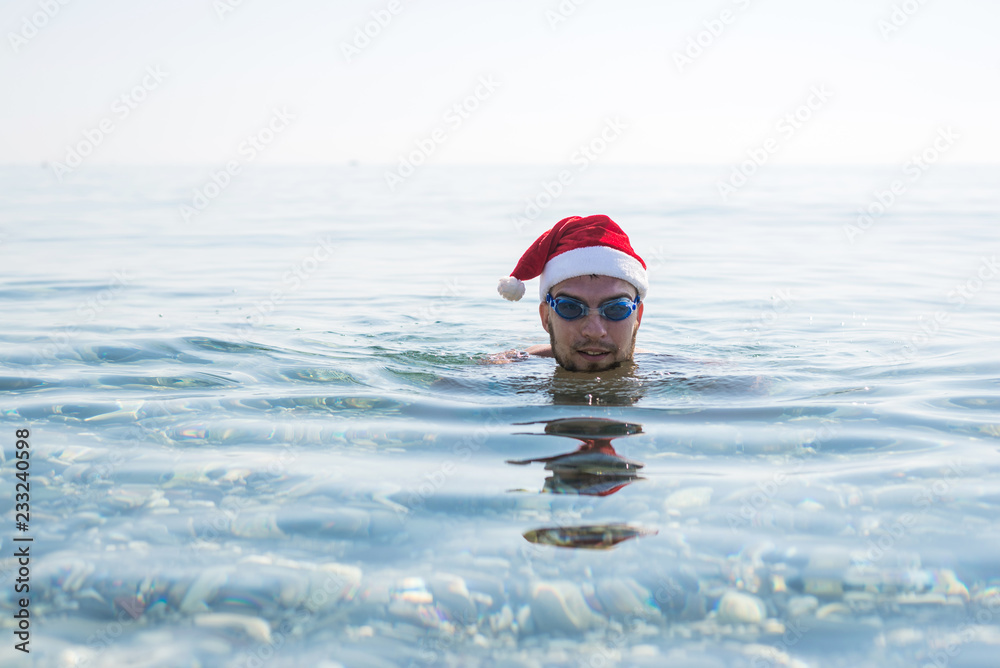 Man in a Santa Claus hat and glasses for swimming, christmas background.