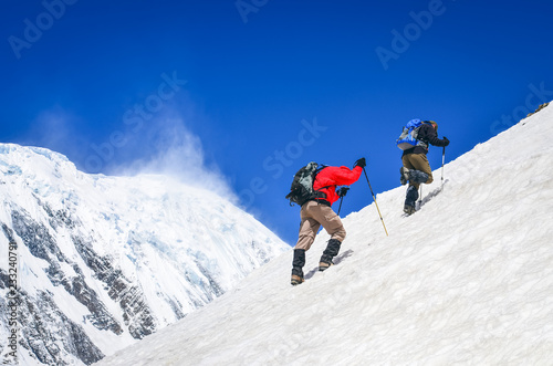 Two mountain trekkers on steep snowed hill with peaks background