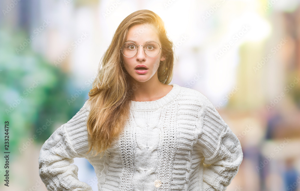 Fototapeta premium Young beautiful blonde woman wearing winter sweater and sunglasses over isolated background afraid and shocked with surprise expression, fear and excited face.