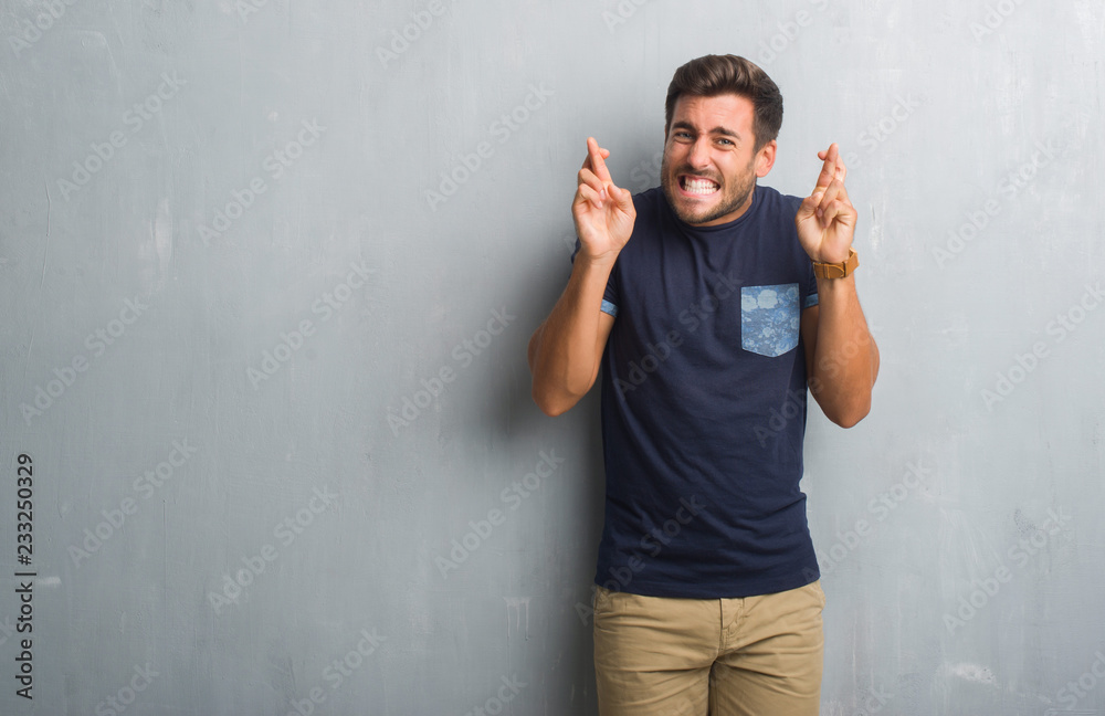 Handsome young man over grey grunge wall smiling crossing fingers with hope and eyes closed. Luck and superstitious concept. Handsome young man over grey grunge wall smiling crossing fingers with hope and eyes closed. Luck and superstitious concept.