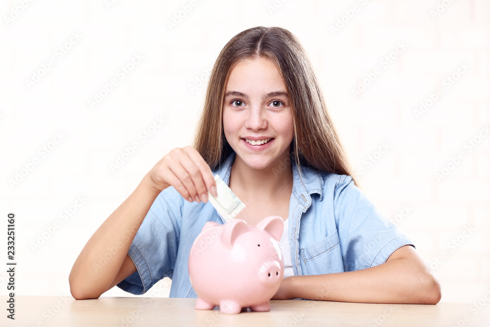 Young girl with pink piggybank and dollar banknote sitting at table Young girl with pink piggybank and dollar banknote sitting at table
