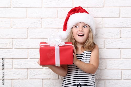 Little girl holding gift box on brick wall background