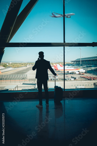 Young businessman looking through the window in the airport talking by telephone