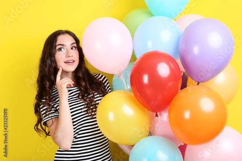 Cute girl with colored balloons on yellow background