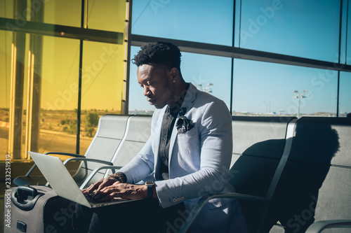 Young businessman is seated in the airport working with a laptop and carrying a suitcase waiting for his flight