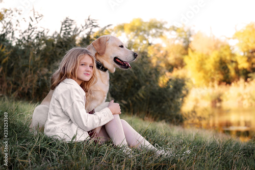 happy little girl with her dog retriever sitting by the river. Cute little girl hugging retriever.