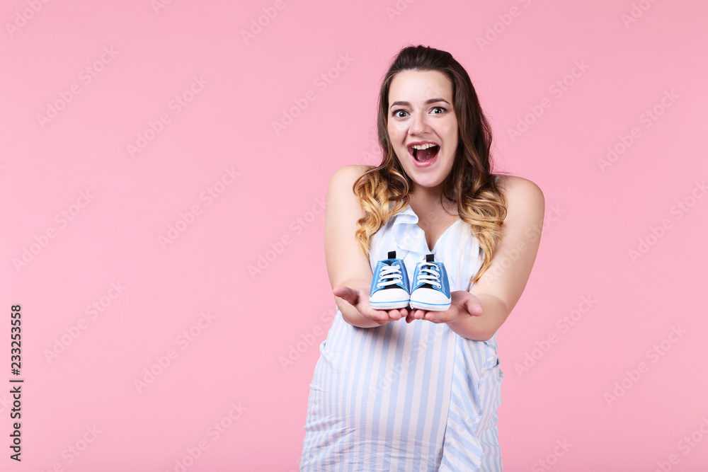 Beautiful pregnant woman with baby shoes on pink background Beautiful pregnant woman with baby shoes on pink background