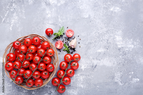 Cherry tomatoes with basil leafs, garlic and spices on grey wooden table